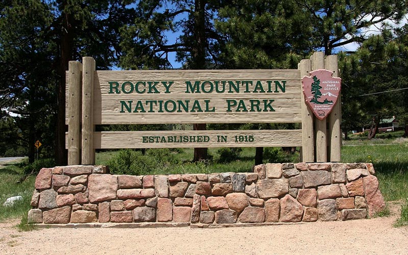 Rocky Mountain National Park entrance sign with trees and mountains in the background.